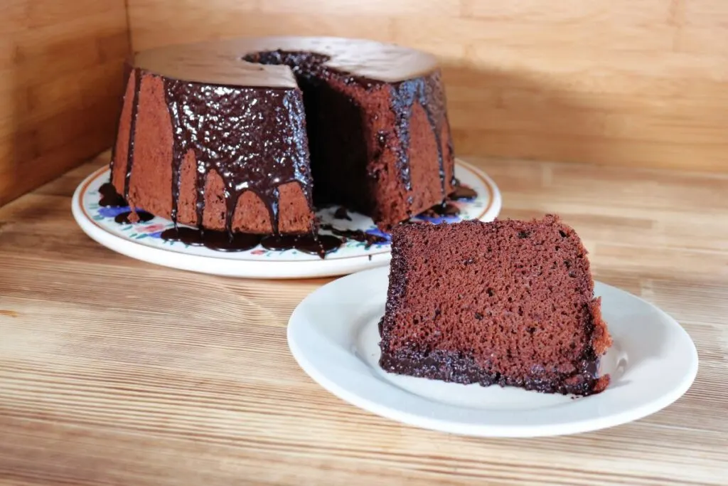 A slice of chocolate chiffon cake sits on a plate. The remaining cake with missing slice sits in the background.