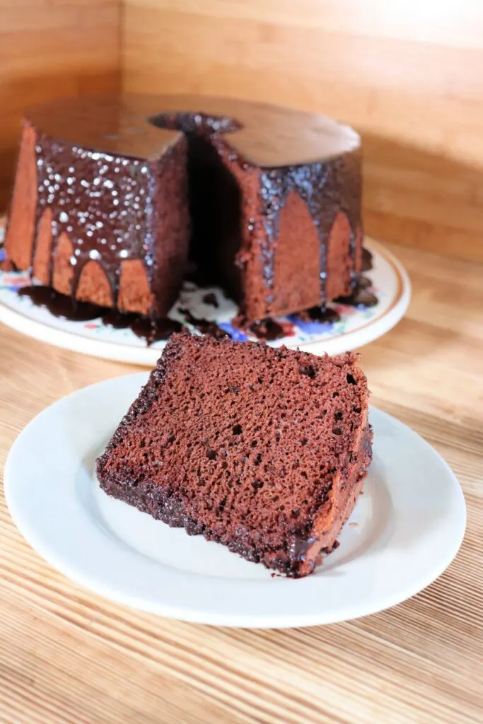 A slice of chocolate chiffon cake sits on a plate. The remaining cake with missing slice sits in the background.