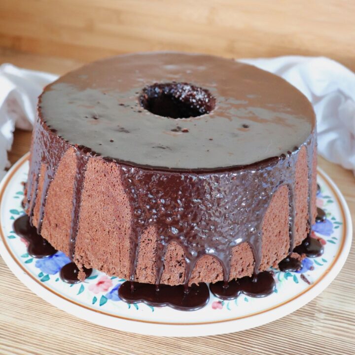 A whole chocolate chiffon cake that has a chocolate glaze sits on a plate.