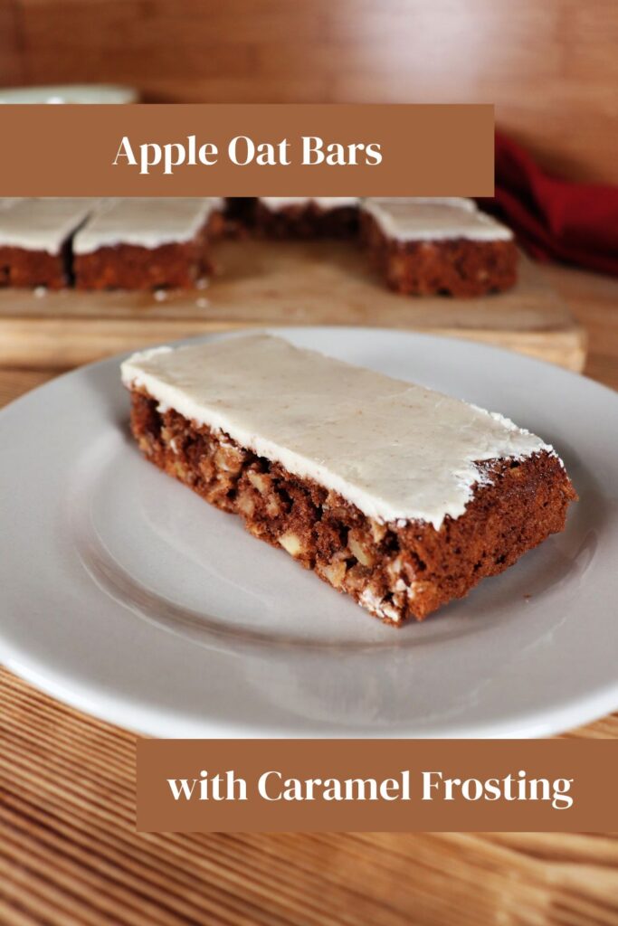 A caramel frosted apple oat bar as seen from the side sits on a white plate. In the background sits a board with more bars on it. Text Overlay reads Apple Oat Bars with Caramel Frosting. 